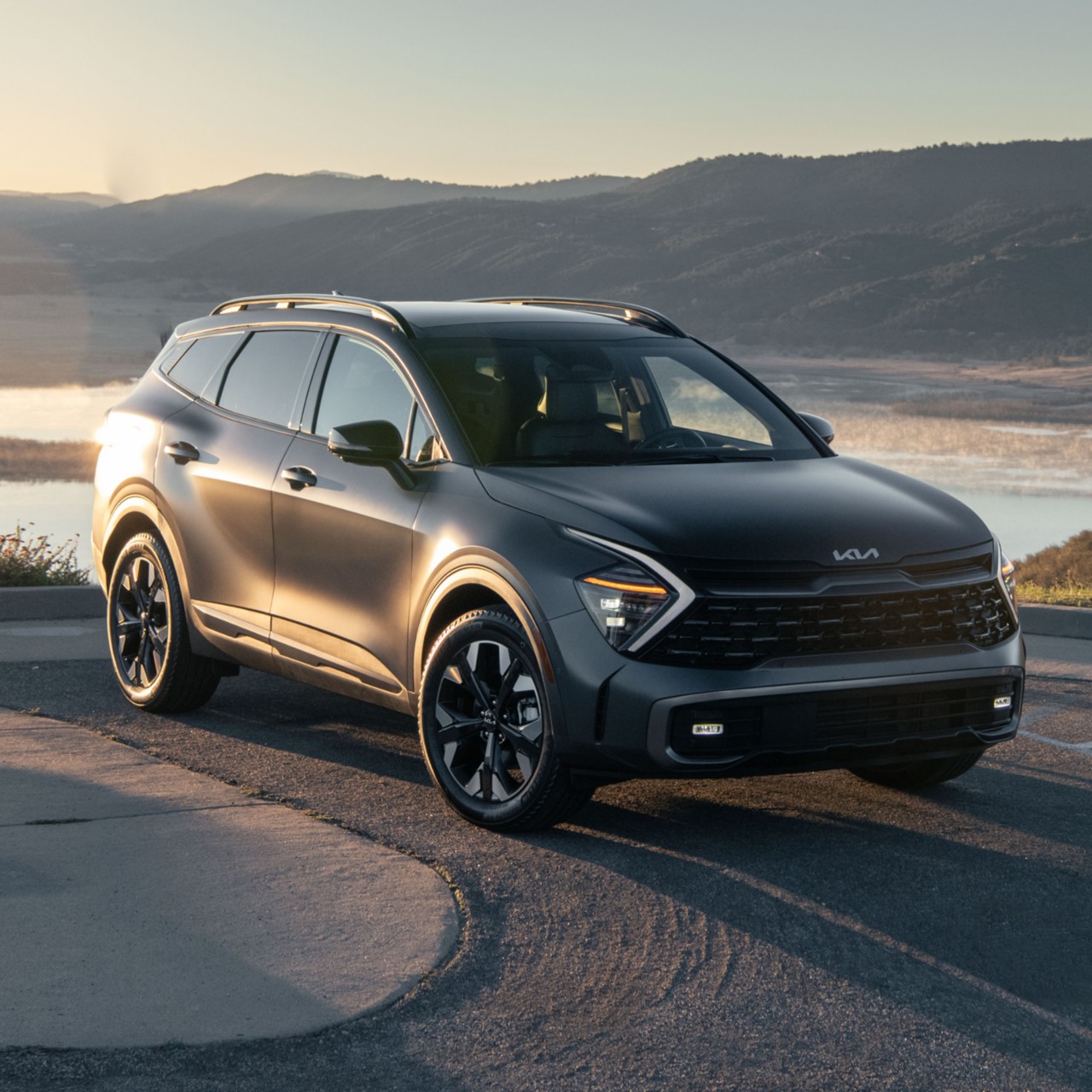2024 Kia Sportage Plug-in Hybrid X-Line Prestige in matte grey, three-quarter front view, parked next to a lake in the mountains