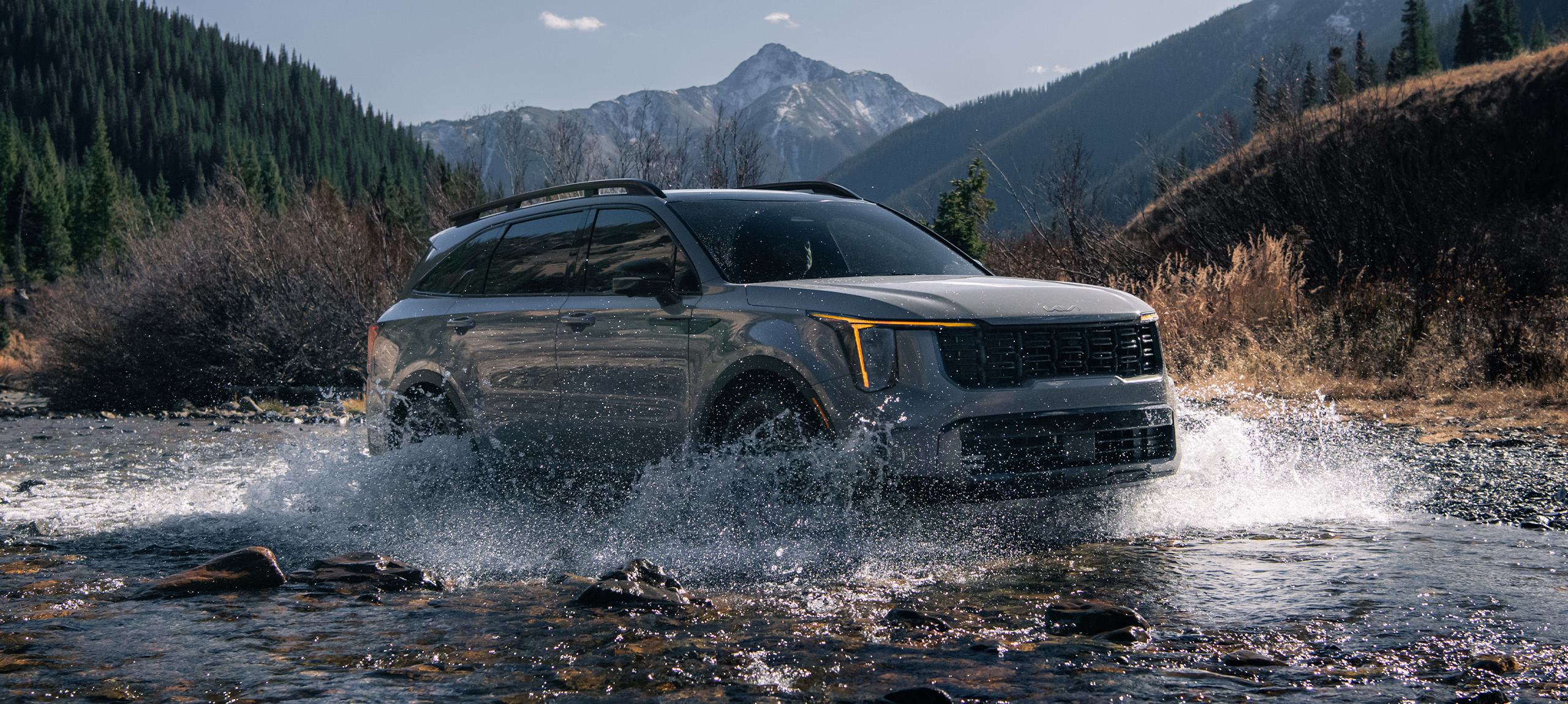2024 Kia Sorento in brown, three-quarter front view, driving through a river of water in the mountains