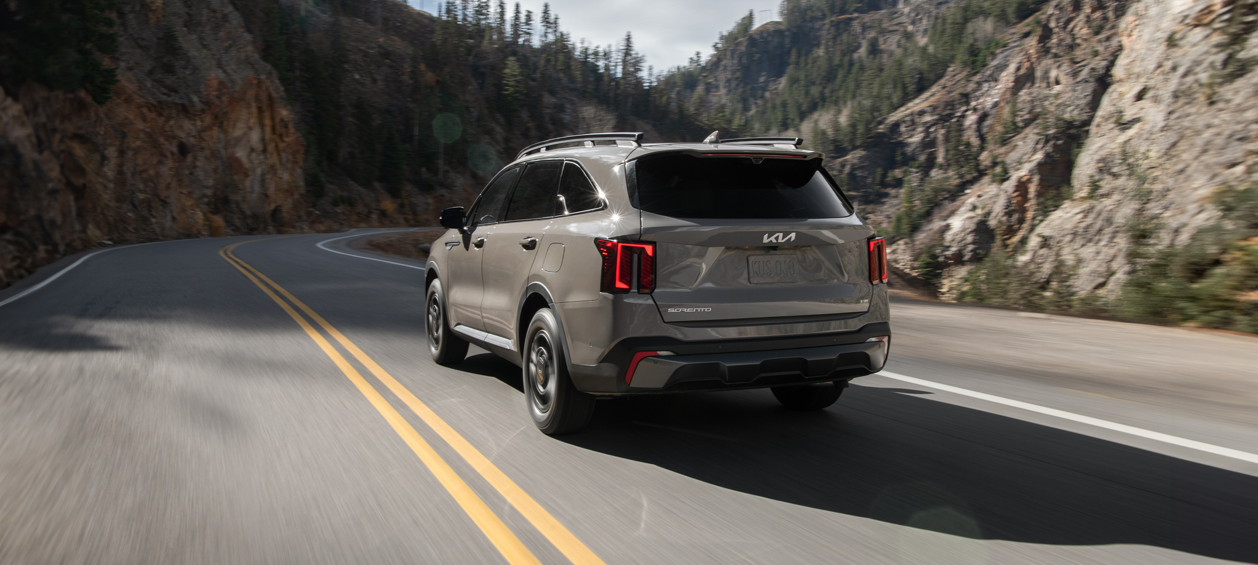 2024 Kia Sorento in brown, three-quarter back view, driving through a winding road in the mountains
