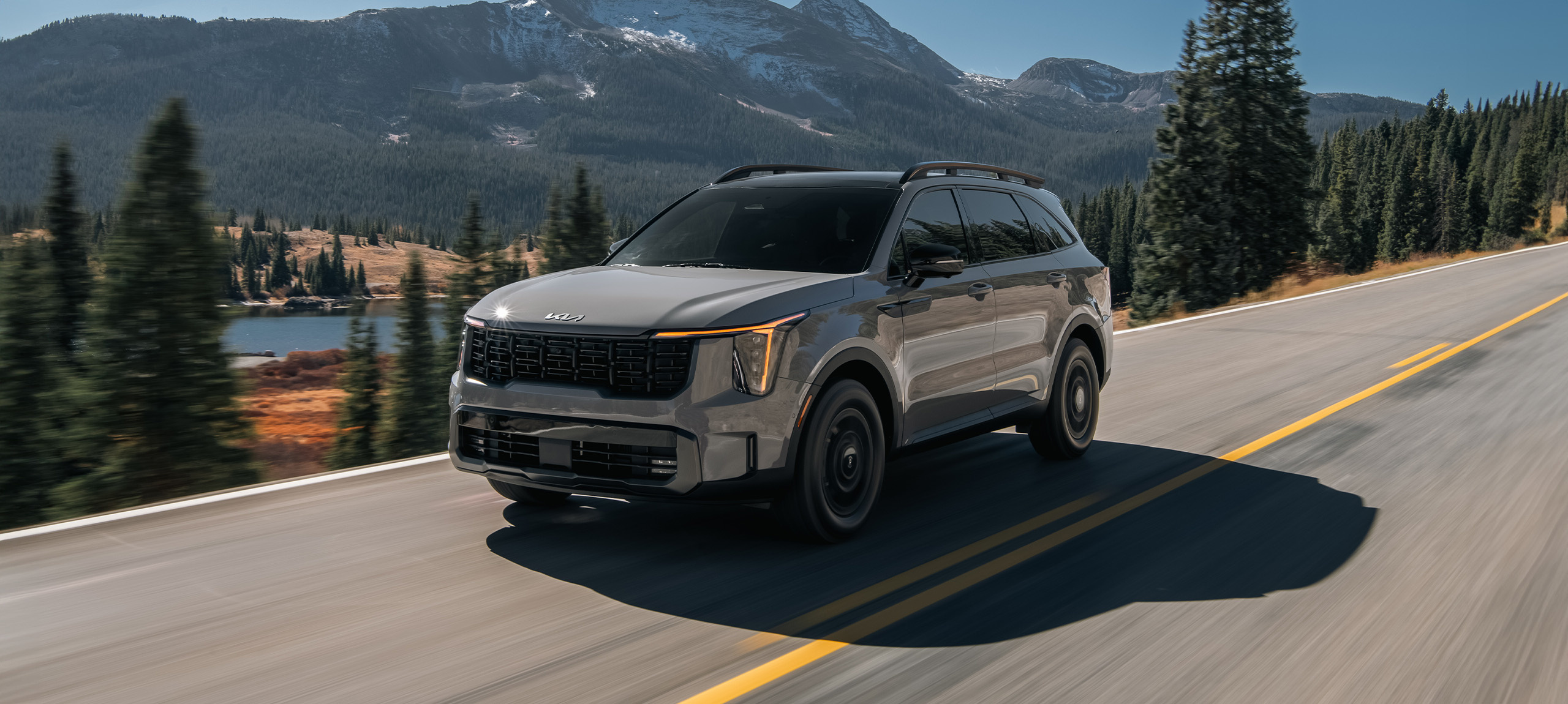 2024 Kia Sorento in a three-quarter front view, driving down a road by the lake in the mountains