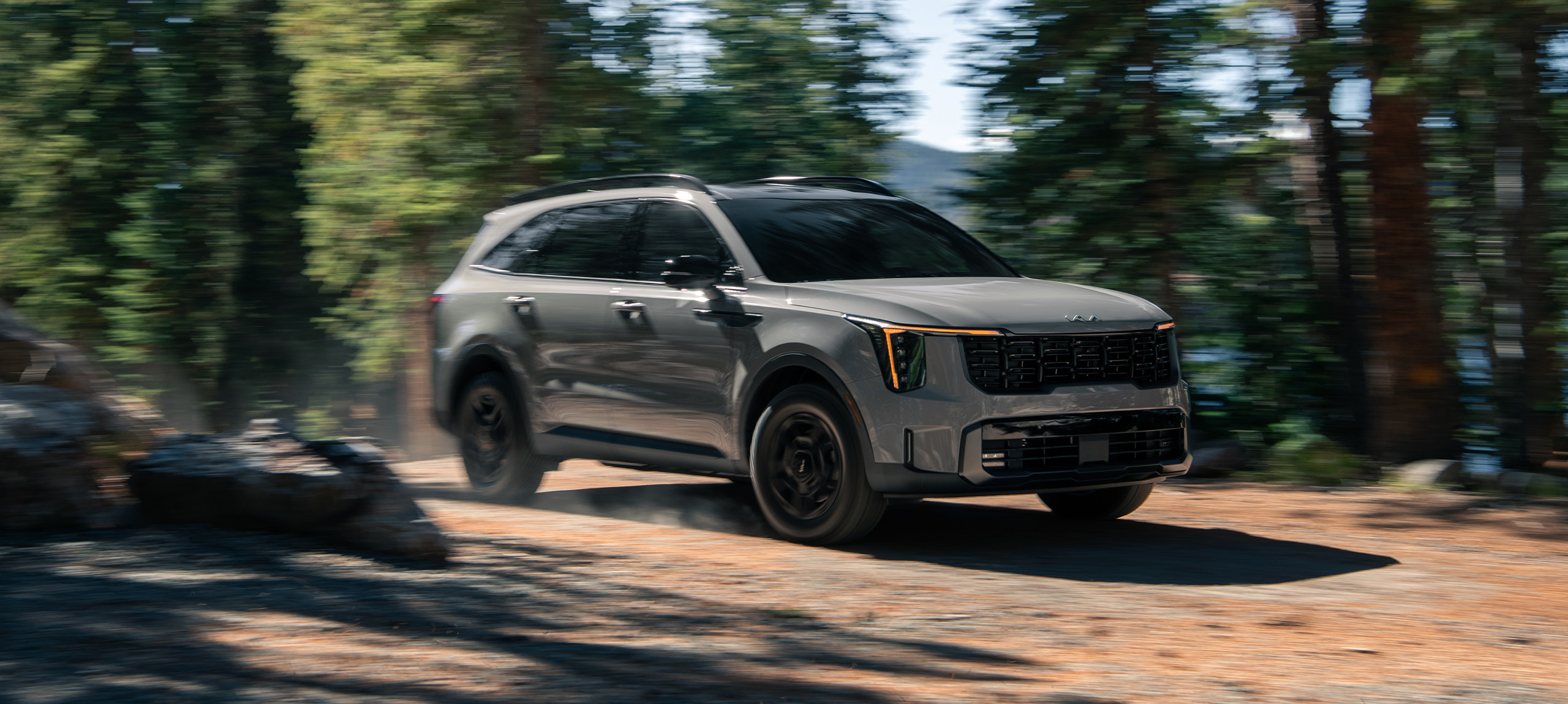 2024 Kia Sorento in brown, three quarter front view, driving through the forest on an unpaved road